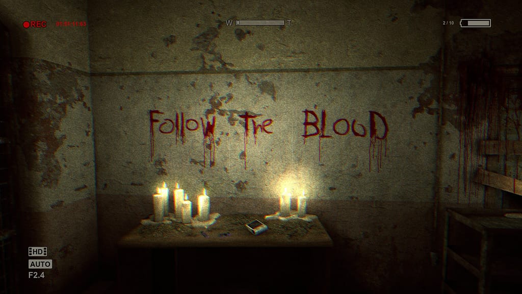Image descriptor: A screenshot from Outlast. From the perspective of a camcorder with various bits of recording UI around the edges of the screen. A table can be seen against a ruined wall; Candles adorning the top of the table. Written in blood on the wall is text that says "Follow the Blood