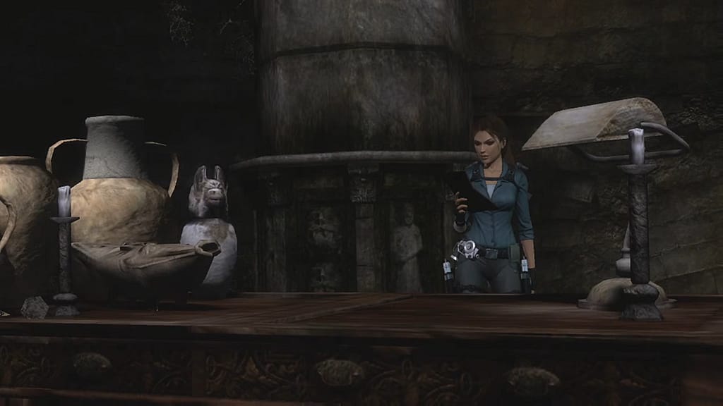 Image Descriptor: A screenshot from Tomb Raider: Underworld's "Beneath the Ashes" DLC. Lara reads a notebook whilst standing next to a large stone column. A desk can be seen in the foreground with a desk lamp and several artefacts resting atop it.