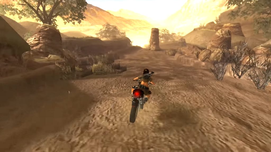 Image Descriptor: Lara rides her motorcycle down a thin desert path, whilst a rock column blocks the way up ahead.