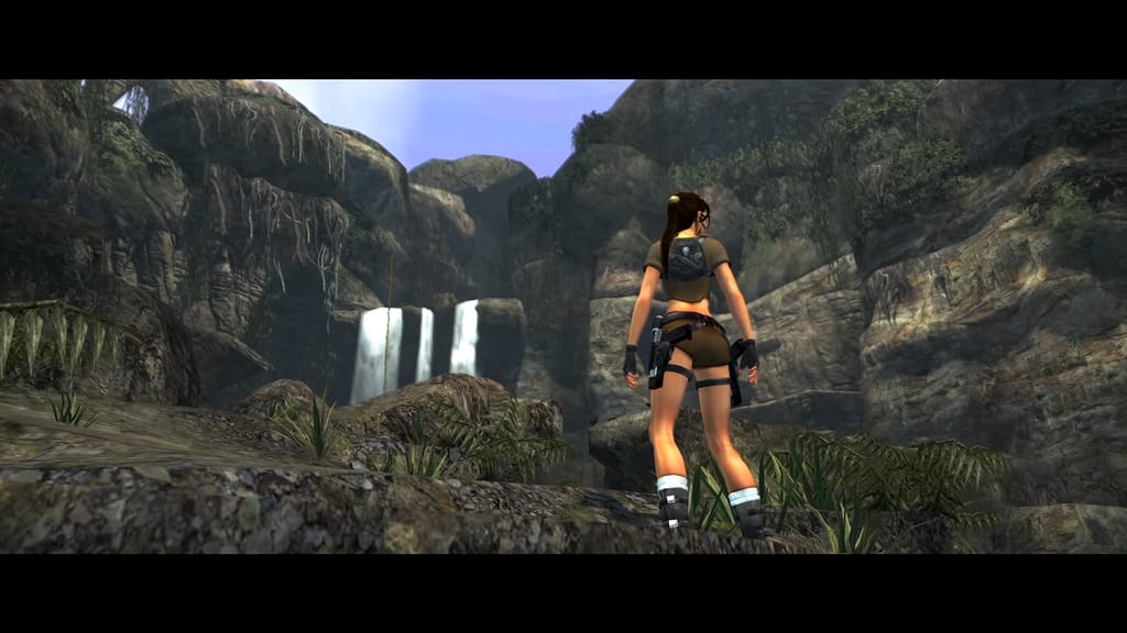 Image Descriptor: Lara stands with her back facing the camera. She is observing her surroundings within a rocky valley, with occasional vines, grass patches and general greenery around her. Several thin water streams can be seen falling from a ledge in the distance.